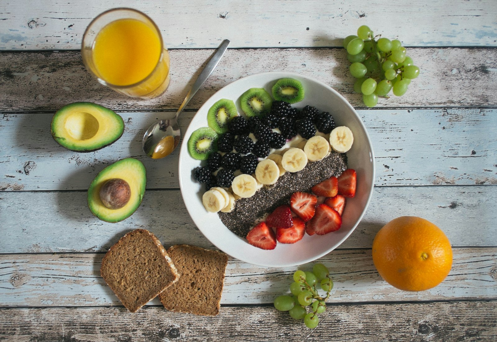 A breakfast bowl of fruit with oranges, avocado and bread on a wooden table